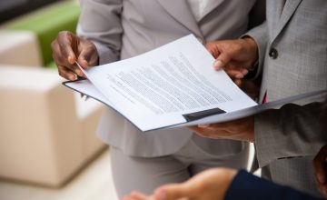 Diverse business partners reading contract together. Business man and woman wearing formal suits, standing and holding open folder with document. Agreement concept